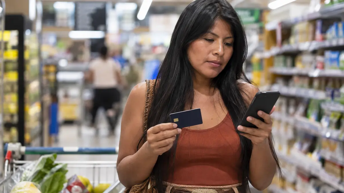 Consumidora consulta o celular e o cartão durante uma compra no supermercado